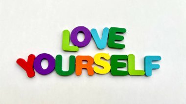 Beyaz arka planda renkli 'Kendini Sev' tahta harfleri.