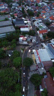 Hava kararırken bir şehir sokağının insansız hava aracı görüntüleri trafik ve yerleşim yerlerini gösteriyor. Araçlar ve evler görülebilir. DKI Jakarta, Endonezya - 30 Aralık 2024