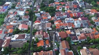 Yoğun bir yerleşim alanının yüksek açılı görüntüsü. Bir sürü ev ve ağaç var. Kırmızı kiremit çatılar belirgin.