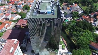 Kanal kenarındaki modern cam gökdelenin yüksek açılı görüntüsü. Etrafı yerleşim binaları ve yemyeşil alanlarla çevrili..