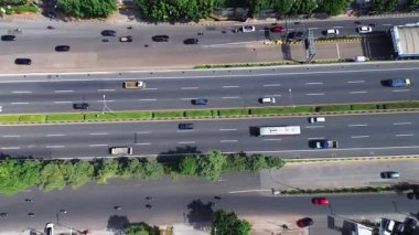 Otoyol trafiğinin yüksek açılı görüntüsü. Arabalar, kamyonlar ve motosikletler çok şeritli bir yol boyunca hareket ederler. Yol kenarındaki yemyeşil ağaçlar.