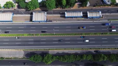 Otoyol trafiğinin yüksek açılı görüntüsü. Arabalar, kamyonlar ve motosikletler çok şeritli yol boyunca hareket ederler. Yemyeşil ağaçlar yan yana dizilir.