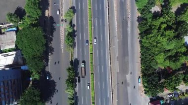 Ağaçlar ve binalar tarafından çevrelenmiş, iki yönde hareket eden arabalar ve motorsikletli, çok şeritli bir şehir yolunun yüksek açılı görüntüsü..
