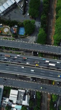 Yoğun trafik, arabalar, kamyonlar ve çevre kentsel manzaralı otoyol kavşağının kuşbakışı görüntüsü.