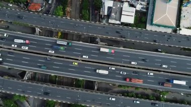 Yoğun trafik akışı, arabalar, kamyonlar ve çevre kentsel manzaralı çok şeritli bir otoyolun yüksek açılı görüntüsü.