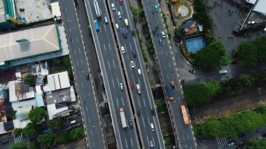 Yoğun otoyol trafiğinin, şehir binalarının ve yemyeşil alanların yüksek açılı görüntüsü. Arabalar, kamyonlar, otobüsler..
