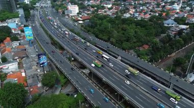 Konut alanları ve yemyeşil yemyeşil ile yoğun trafiği olan çok şeritli bir otobanın yüksek açılı görüntüsü. DKI Jakarta, Endonezya - 09 Januari 2025