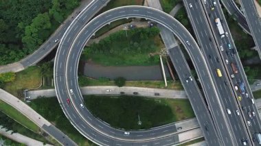 Yoğun bir otoyol kavşağının insansız hava aracı görüntüleri dairesel rampalar ve yoğun trafik akışı. Yeşiller yolların etrafını sarmış..