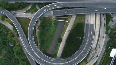Hareket halindeki arabalar ve kamyonlar ile yoğun bir otoyol kavşağının tepe noktası. Yolları çevreleyen yemyeşil alanlar.
