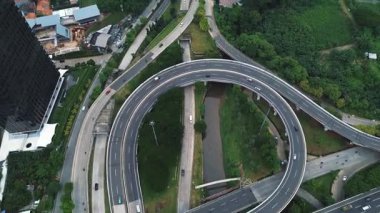 Kentsel ve yeşil alanlarla çevrili yoğun trafik ile bir otoyol kavşağının insansız hava aracı görüntüleri.