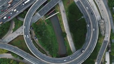 Trafik ve yeşil alanlarla dolu yoğun bir otoyol kavşağının yukarıdan çekimleri. Arabalar, kamyonlar ve motosikletler..