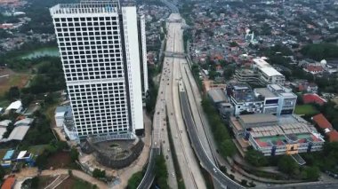 Yoğun bir otoyol kavşağının, gökdelenlerin ve kentsel manzaranın yüksek açılı görüntüsü. Karmaşık yol sisteminden arabalar ve kamyonlar geçiyor. DKI Jakarta, Endonezya - 11 Ocak 2025