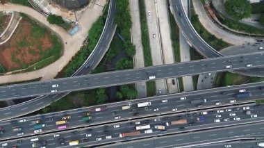 Araçlar, kamyonlar ve çevre şehir altyapısı ile yoğun bir otoyol kavşağının insansız hava aracı görüntüsü..