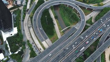 Yoğun bir karayolu kavşağının hava aracı görüntüsü yoğun trafik akışı ile çevrili yemyeşil şehir manzarası.