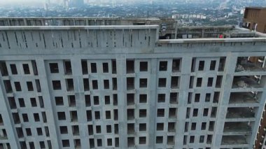 İnşaat halindeki büyük, tamamlanmamış bir binanın yüksek açılı görüntüleri. Somut yapı, boş pencere çerçeveleri, şehir manzarası.
