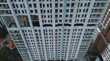 İnşaat halindeki büyük bir apartmanın insansız hava aracı görüntüleri. Beton yapı, boş pencere çerçeveleri ve çevreleyen alanı gösterir.