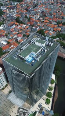 Geleneksel evleri olan yoğun bir şehirle çevrili modern bir gökdelenin insansız hava aracı görüntüleri. Bulutlu gökyüzü.