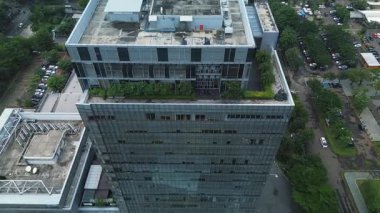Otoparklar ve yemyeşil ağaçlarla çevrili modern bir ofis binasının insansız hava aracı görüntüleri. Yüksek katlı şehir manzarası. DKI Jakarta, Endonezya - 22 Ocak 2025