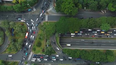 Yoğun şehir trafiğini, arabaları ve motosikletleri karmaşık bir kavşakta yüksek açılı görüyor. Yolları çevreleyen yemyeşil ağaçlar..