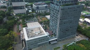 Yeşillik ve otoparklarla çevrili modern bir ofis binasının insansız hava aracı görüntüleri. İki bina ve çevreyi gösteriyor. DKI Jakarta, Endonezya - 22 Ocak 2025