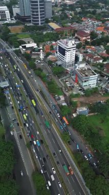 Yoğun bir otoyolun yüksek açılı görüntüsü arabalar, otobüsler ve binalar. Yol boyunca yemyeşil ağaçlar var..