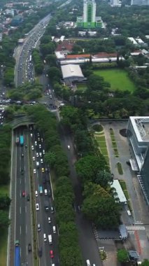 Yoğun trafiği olan, yemyeşil ağaçlar ve binalarla çevrili işlek bir şehir otoyolunun yüksek açılı görüntüsü..