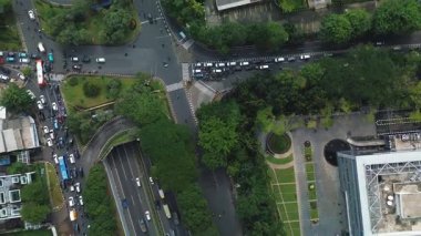 Yoğun trafik akışıyla dolu, yemyeşil ağaçlar ve binalarla çevrili işlek bir şehir kavşağının yüksek açılı görüntüsü.
