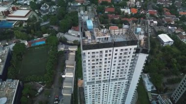 Yoğun bir şehir manzarasının ortasında, yemyeşil ve yerleşim alanlarıyla çevrili modern bir gökdelenin insansız hava aracı görüntüleri..