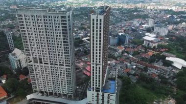 İnşaat halindeki iki yüksek binanın insansız hava aracı görüntüleri. Yoğun bir şehir ve yemyeşil alanla çevrili..