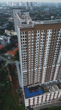 İnşaat halindeki bir binanın yanındaki, şehirle çevrili, uzun ve modern bir apartmanın drone görüntüleri..