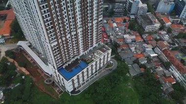 Çağdaş bir apartmanın insansız hava aracı görüntüleri yemyeşil bir bölgenin ve yerleşim yerinin yanında..