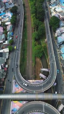 Otoyol ve yerleşim alanının yanından geçen bir trenin insansız hava aracı görüntüleri. Araçlar yemyeşil bitki örtüsünün yanında, yollarda ilerler. DKI Jakarta, Endonezya - 25 Ocak 2025