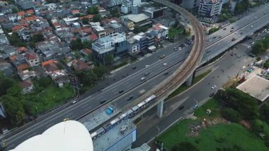Yoğun trafiğin ortasında üst geçitten geçen bir MRT treninin yüksek açılı görüntüsü. Şehir manzarası arkaplanı.