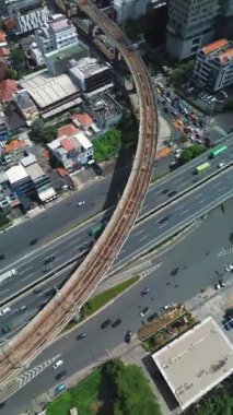 Yoğun bir otoyolda, kentsel binalar ve yemyeşil alanlarla çevrili bir MRT tren hattının yüksek açılı görüntüsü..