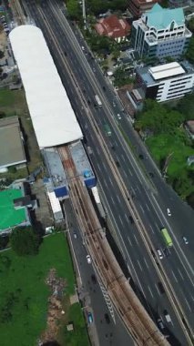 Yoğun bir otoyolu kesen MRT tren raylarının yüksek açılı görüntüsü, şehir binaları ve yeşilliklerle çevrili..