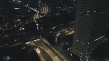 Gece şehir otobanının hava görüntüsü, trafik akışını ve şehir ışıklarını gösteriyor. Arabalar ve binalar görünür.