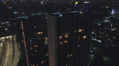 Gece vakti iki modern gökdelenin havadan çekilmiş görüntüleri karanlık bir şehrin arka planına karşı aydınlatılmış pencereler. Aşağıda trafik görülebilir.