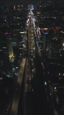 Trafiğin sorunsuz aktığı işlek bir şehir otoyolunun gece vakti hava görüntüsü. Parlak şehir ışıkları manzarayı aydınlatır.