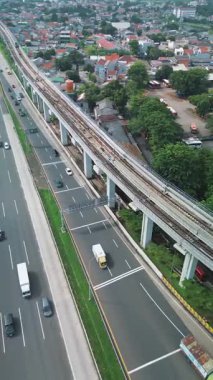 Bir otoyolun ve paralel giden yükseltilmiş tren raylarının, yerleşim alanları ve bir otobüs durağının hava görüntüleri..