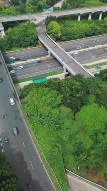 Yoğun trafik ve yemyeşil ağaçlarla üst geçidin yüksek açılı görüntüsü. Arabalar, kamyonlar ve motosikletler..