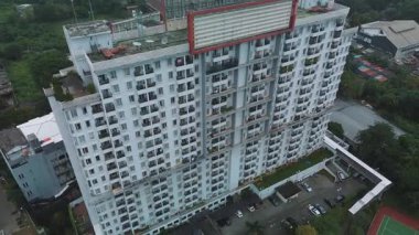 Geniş, modern bir apartmanın yüksek açılı insansız hava aracı görüntüsü. Otoparkı ve çevresi yeşil..