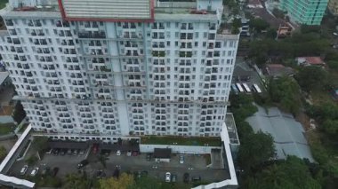 Modern bir apartmanın, otoparkın ve çevreleyen yeşilliğin yüksek açılı insansız hava aracı görüntüleri. Statik kamera.