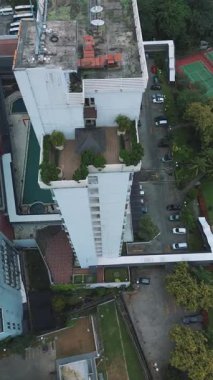 Yüksek bir binanın, çatı havuzunun, otoparkın ve çevreleyen yeşilliğin drone görüntüleri. Tepeden çekim.