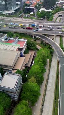 Yoğun trafik, binalar ve yemyeşil ağaçlarla şehir otobanının yüksek açılı görüntüsü.