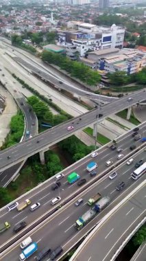 Yoğun şehir otoyolu trafiğinin yüksek açılı insansız hava aracı görüntüleri, arabalar, kamyonlar ve otobüsleri gösteriyor. Üstgeçit ve çevresindeki binalar görünür..