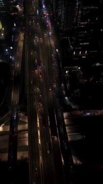 Gece trafiğinin yüksek açılı görüntüsü. Arabalar birden fazla şeritte gider. Arka planda görünen şehir binaları.