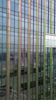 Şehir manzarasını yansıtan modern cam bir binanın dış görüntüsü. Statik çekim, dikey çerçeve.