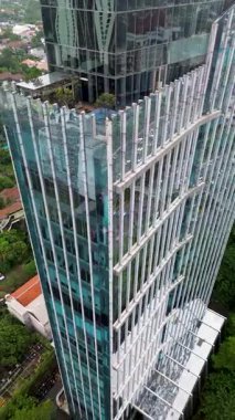 Yeşillik ve şehir trafiği ile çevrili modern cam gökdelenin yüksek açılı görüntüsü. Dikey görünüm.