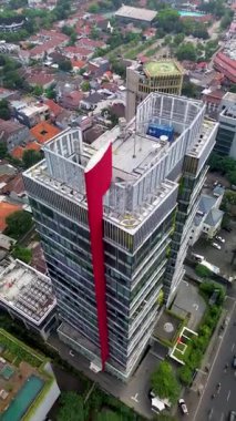 Yoğun bir şehirde, yerleşim binaları ve işlek bir yol ile çevrili modern bir gökdelenin yüksek açılı insansız hava aracı görüntüleri..