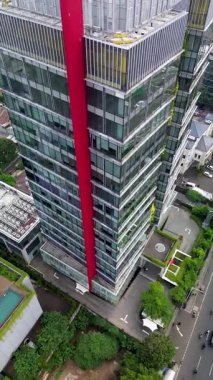 Şehir binaları ve caddelerle çevrili, belirgin kırmızı dikey aksanlı modern cam gökdelenin yüksek açılı görüntüsü..